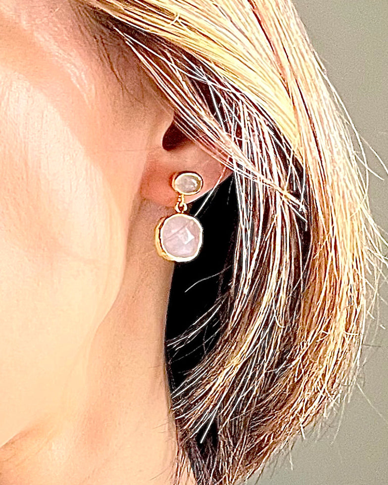 Close-up of a person wearing a gold earring with a pink gemstone.